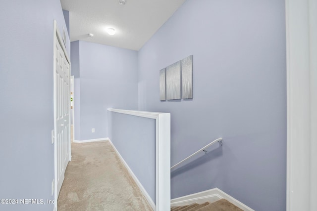 hallway with vaulted ceiling, a textured ceiling, and light colored carpet