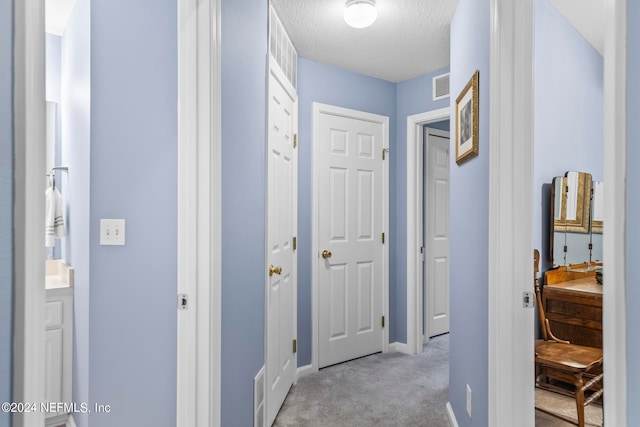 hallway featuring a textured ceiling and light colored carpet