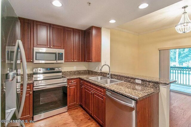 kitchen with stainless steel appliances, decorative light fixtures, sink, kitchen peninsula, and light hardwood / wood-style flooring