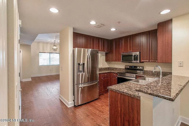 kitchen with dark stone counters, appliances with stainless steel finishes, sink, hardwood / wood-style floors, and kitchen peninsula