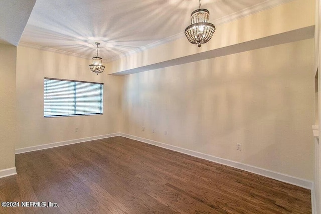 empty room featuring dark wood-type flooring, a chandelier, and ornamental molding