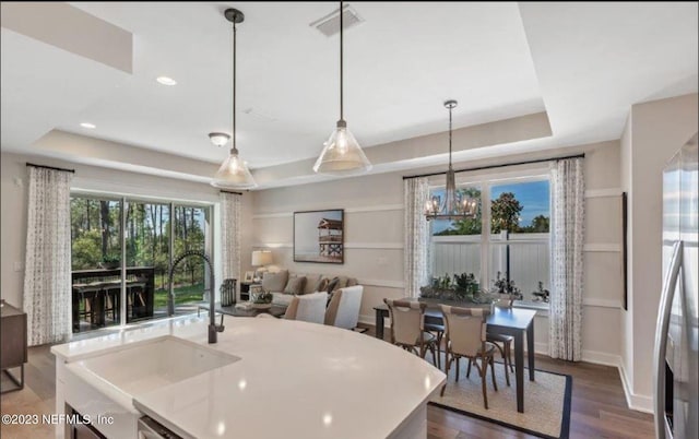 kitchen featuring a raised ceiling, sink, hanging light fixtures, dark hardwood / wood-style floors, and an island with sink