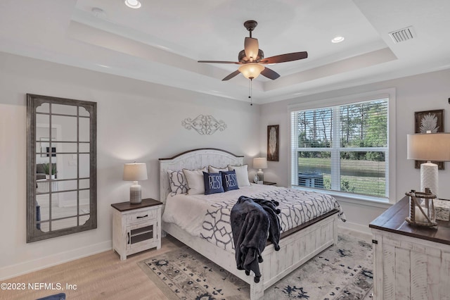 bedroom with light hardwood / wood-style floors, a raised ceiling, ceiling fan, and ornamental molding