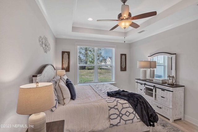 bedroom with a raised ceiling, multiple windows, ceiling fan, and light hardwood / wood-style flooring