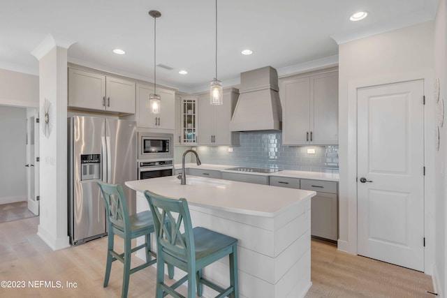 kitchen with sink, an island with sink, light wood-type flooring, appliances with stainless steel finishes, and custom exhaust hood