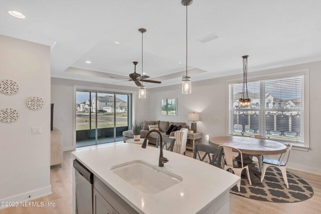 kitchen featuring stainless steel dishwasher, a tray ceiling, sink, pendant lighting, and an island with sink