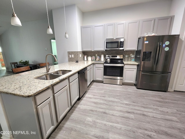 kitchen with pendant lighting, sink, kitchen peninsula, stainless steel appliances, and light stone countertops