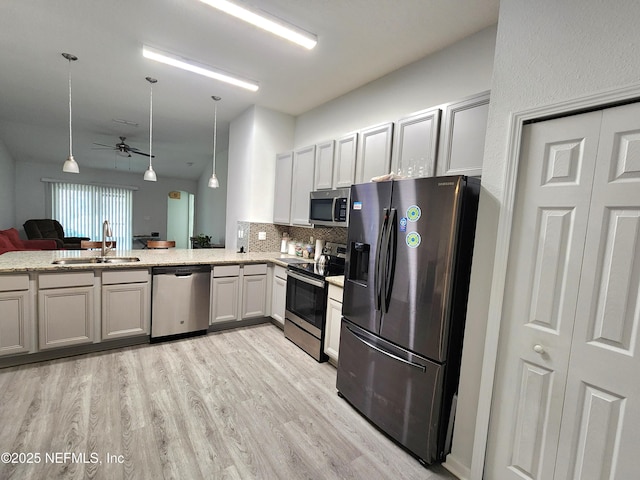 kitchen with appliances with stainless steel finishes, pendant lighting, sink, light hardwood / wood-style floors, and kitchen peninsula