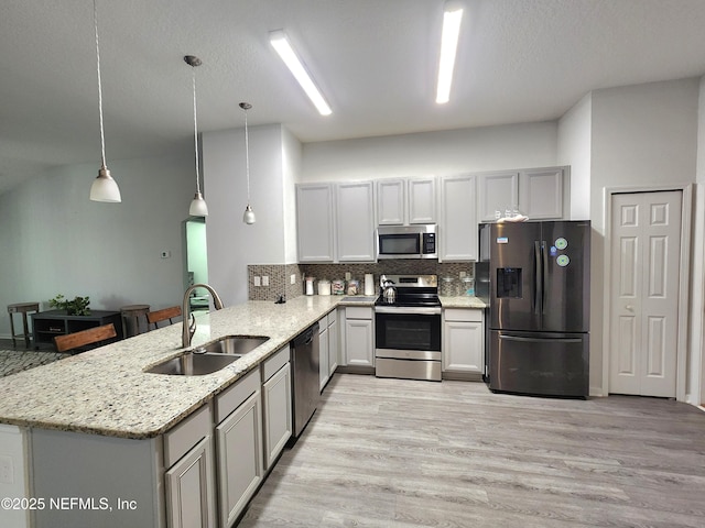 kitchen with sink, hanging light fixtures, kitchen peninsula, stainless steel appliances, and light stone countertops