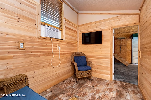 living area with cooling unit, wood walls, ornamental molding, a textured ceiling, and vaulted ceiling