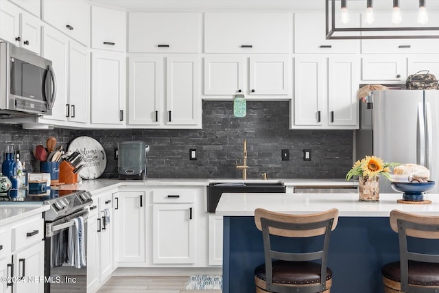 kitchen with decorative backsplash, sink, white cabinetry, appliances with stainless steel finishes, and a kitchen breakfast bar