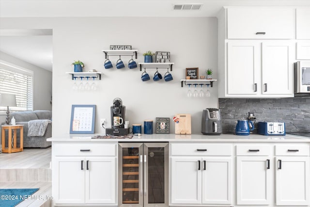 bar featuring light wood-type flooring, beverage cooler, backsplash, and white cabinets