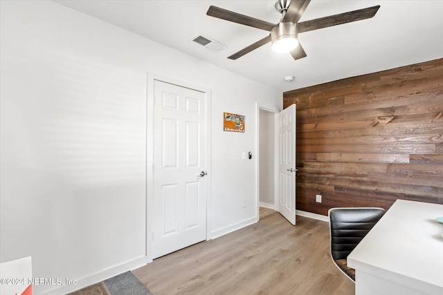 unfurnished office with light wood-type flooring, wooden walls, and ceiling fan