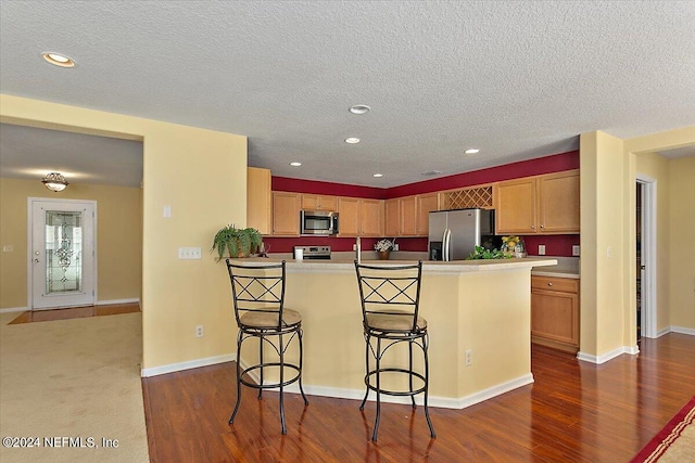 kitchen featuring dark wood-type flooring, appliances with stainless steel finishes, a kitchen bar, and a kitchen island