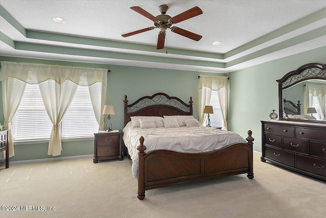 carpeted bedroom with a textured ceiling, a tray ceiling, and ceiling fan