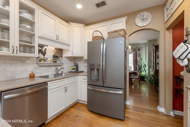 kitchen with sink, backsplash, white cabinetry, stainless steel appliances, and light wood-type flooring