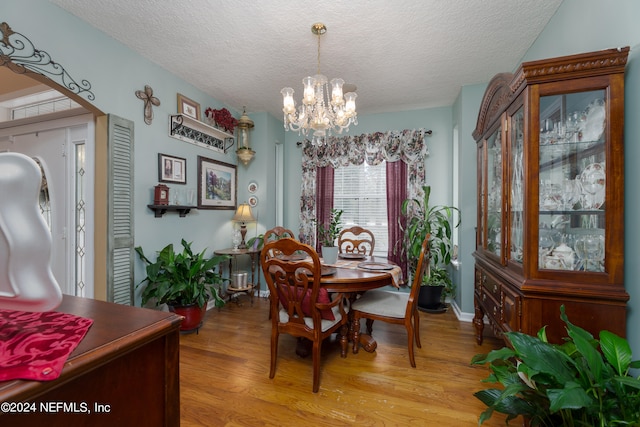 dining space with a textured ceiling, a notable chandelier, and light hardwood / wood-style flooring