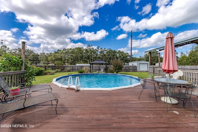 view of pool with a gazebo, a wooden deck, a storage unit, and a lawn