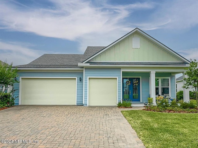 view of front of house featuring covered porch, a garage, decorative driveway, board and batten siding, and a front yard