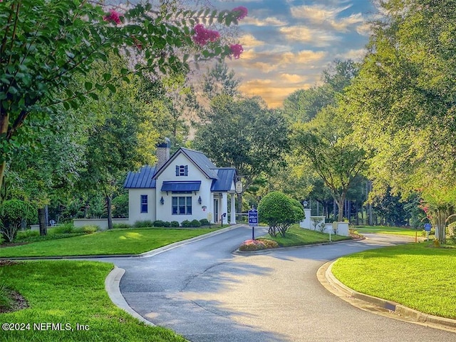 view of front of property with metal roof, driveway, a front lawn, a standing seam roof, and a chimney