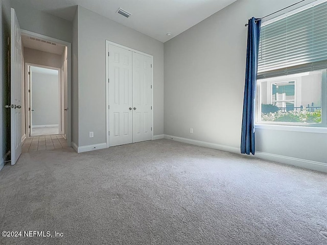 unfurnished bedroom featuring a closet, light colored carpet, visible vents, and baseboards