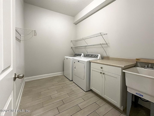 laundry room featuring light wood-style flooring, a sink, baseboards, cabinet space, and washing machine and clothes dryer