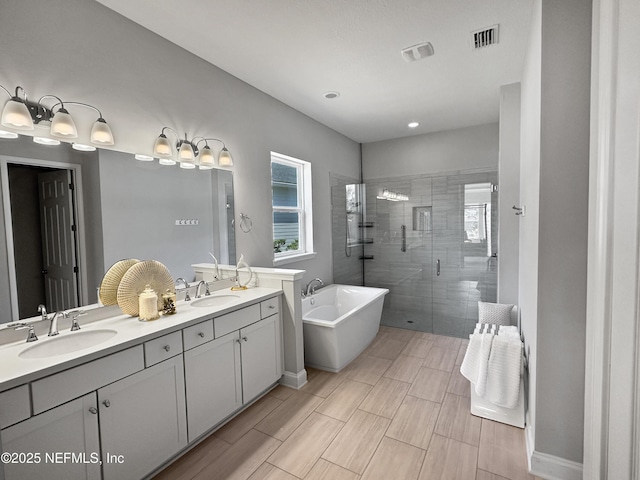 bathroom featuring a stall shower, a freestanding tub, visible vents, and a sink