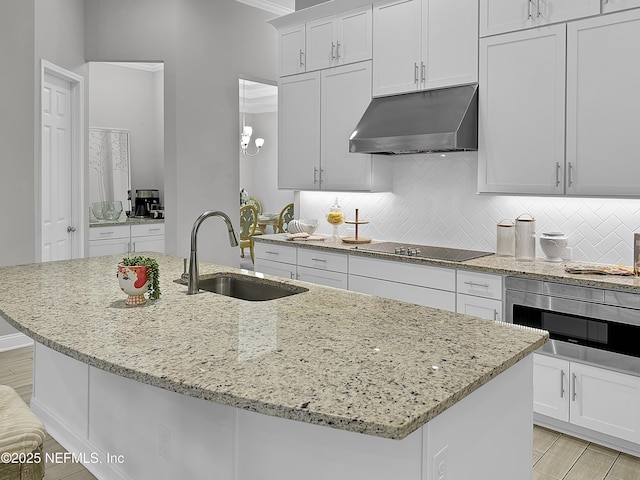 kitchen featuring white cabinets, a kitchen island with sink, a sink, under cabinet range hood, and black electric cooktop