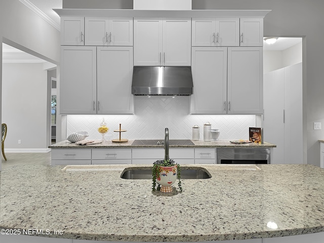 kitchen with a sink, wall chimney range hood, light stone countertops, tasteful backsplash, and crown molding