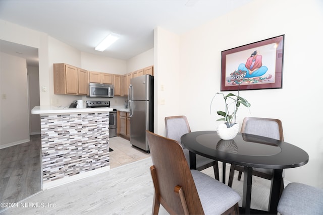 kitchen with kitchen peninsula, light brown cabinets, appliances with stainless steel finishes, and light hardwood / wood-style flooring