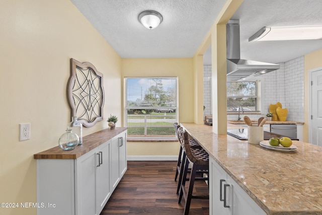 kitchen with light stone countertops, wall chimney exhaust hood, dark hardwood / wood-style floors, a textured ceiling, and white cabinets