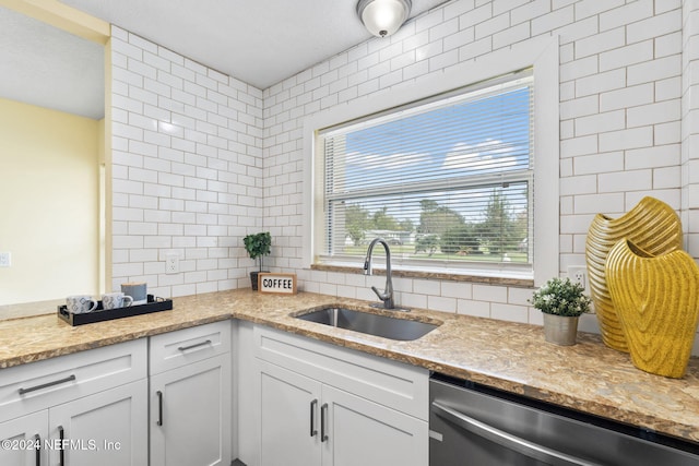 kitchen featuring white cabinetry, sink, light stone counters, dishwasher, and decorative backsplash