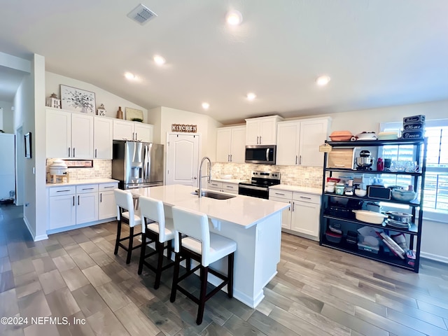 kitchen featuring light wood-type flooring, stainless steel appliances, an island with sink, lofted ceiling, and white cabinetry