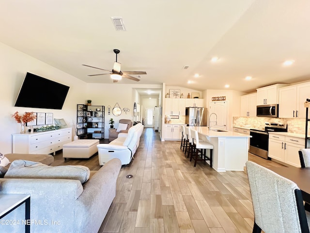 living room featuring lofted ceiling, ceiling fan, sink, and light hardwood / wood-style flooring