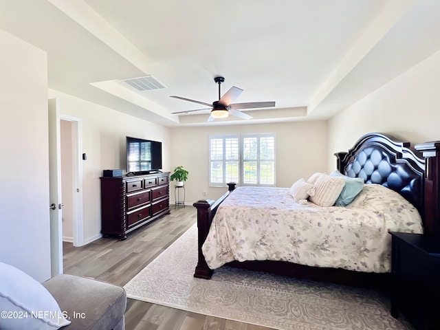 bedroom featuring ceiling fan, a raised ceiling, and light hardwood / wood-style flooring