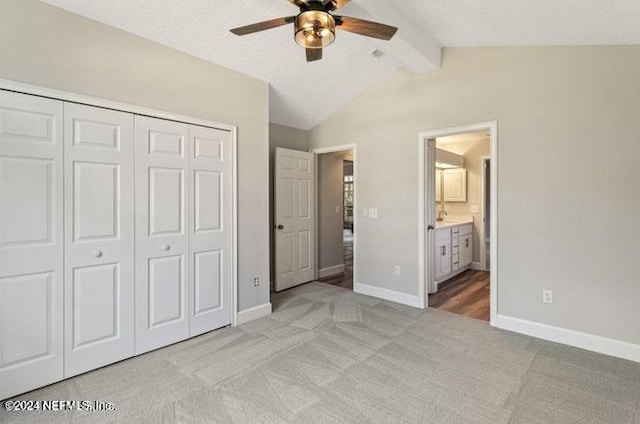 unfurnished bedroom featuring a closet, vaulted ceiling with beams, light carpet, ceiling fan, and ensuite bathroom