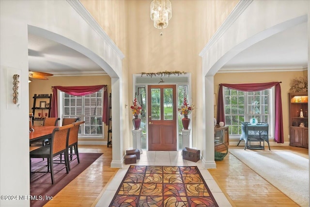 entryway featuring crown molding, light hardwood / wood-style floors, a towering ceiling, and a notable chandelier