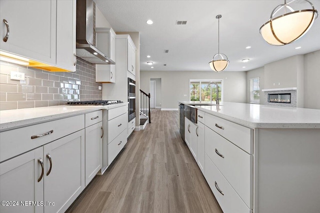 kitchen featuring hanging light fixtures, light hardwood / wood-style floors, wall chimney range hood, and white cabinets