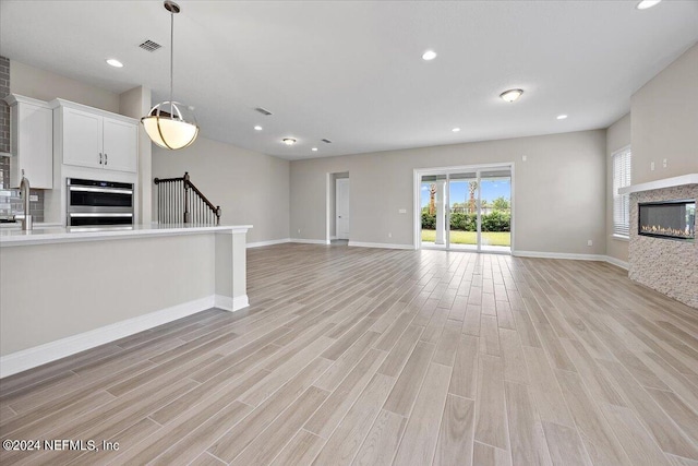 unfurnished living room with sink, a multi sided fireplace, and light hardwood / wood-style floors