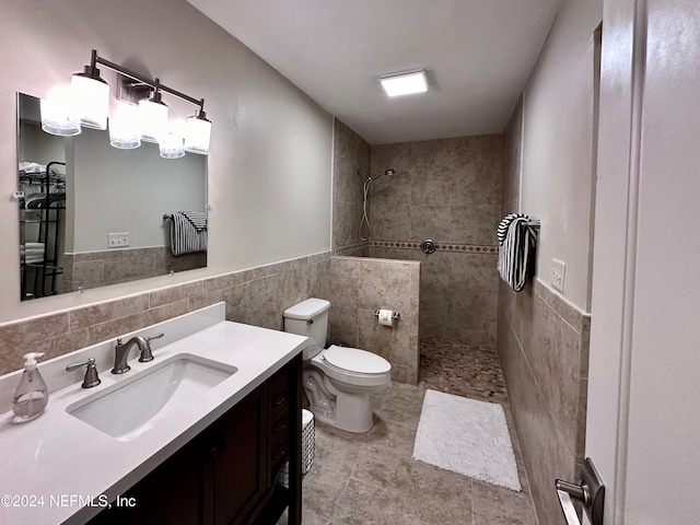 bathroom with vanity, tile patterned flooring, toilet, tiled shower, and tile walls