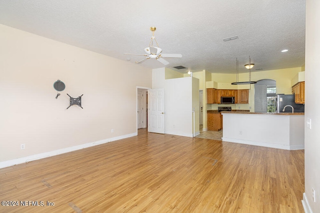 unfurnished living room with ceiling fan, a textured ceiling, and light wood-type flooring