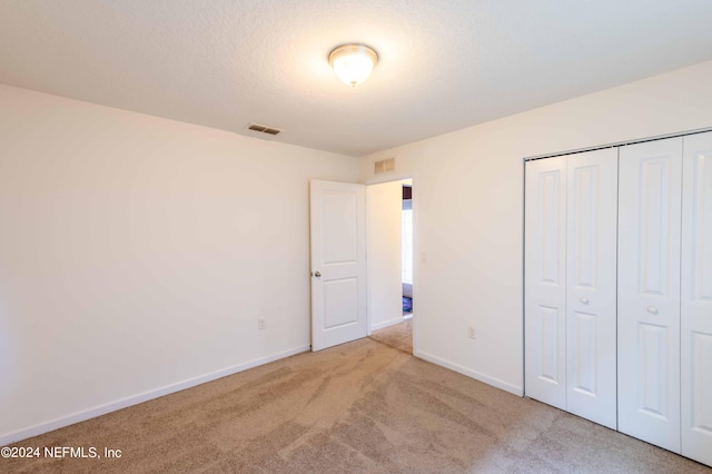 unfurnished bedroom with a textured ceiling, light carpet, and a closet