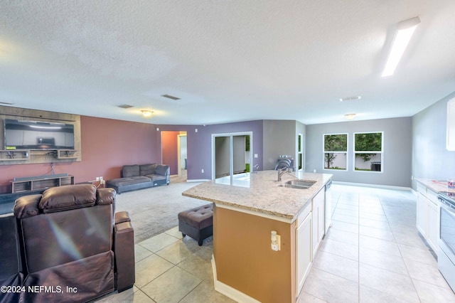 kitchen with light tile patterned floors, light stone counters, a textured ceiling, and a kitchen island with sink