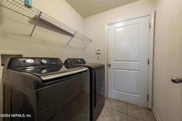 laundry room featuring a textured ceiling, light tile patterned floors, and washing machine and clothes dryer