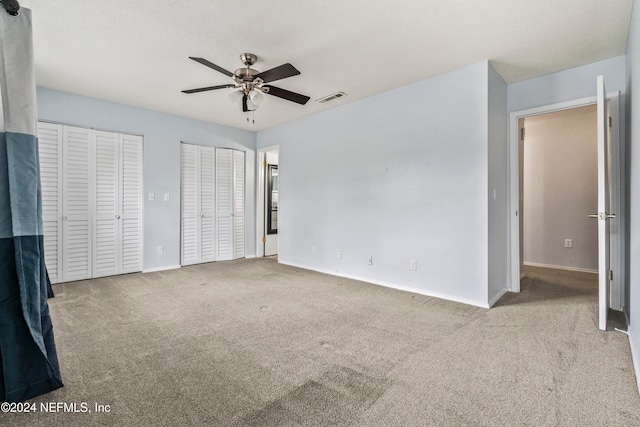 unfurnished bedroom featuring ceiling fan, multiple closets, and light colored carpet