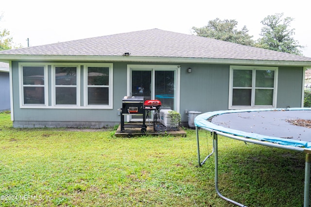 back of house with a trampoline and a lawn