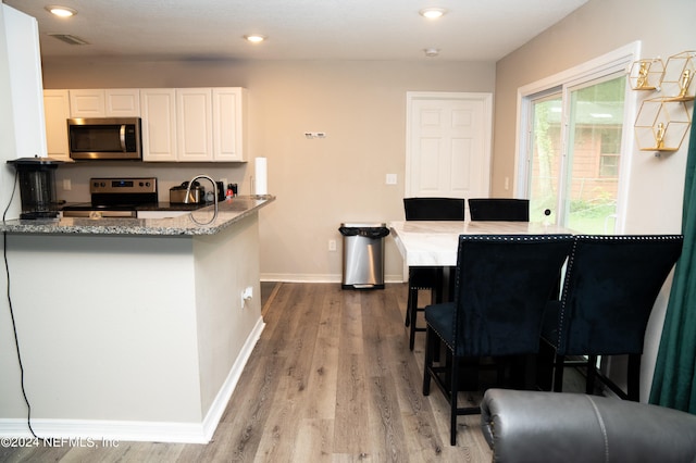 kitchen featuring a breakfast bar, white cabinetry, kitchen peninsula, appliances with stainless steel finishes, and light stone countertops