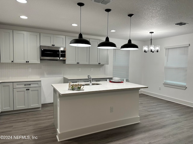 kitchen with hanging light fixtures, sink, an island with sink, and dark hardwood / wood-style flooring