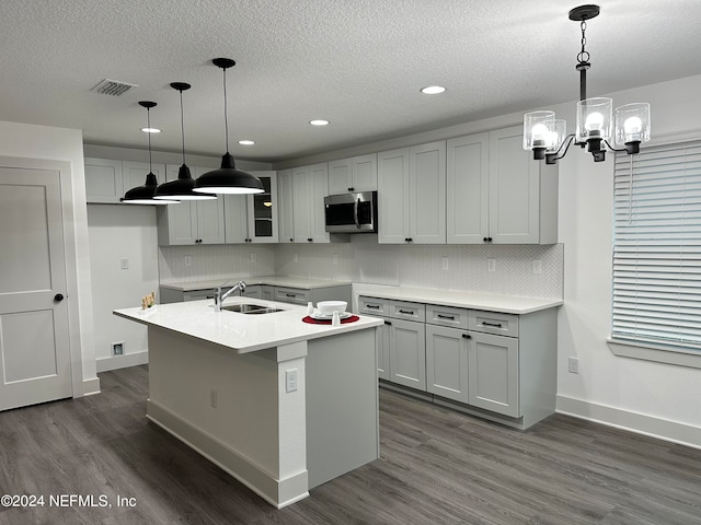 kitchen with pendant lighting, dark hardwood / wood-style floors, sink, backsplash, and a center island with sink