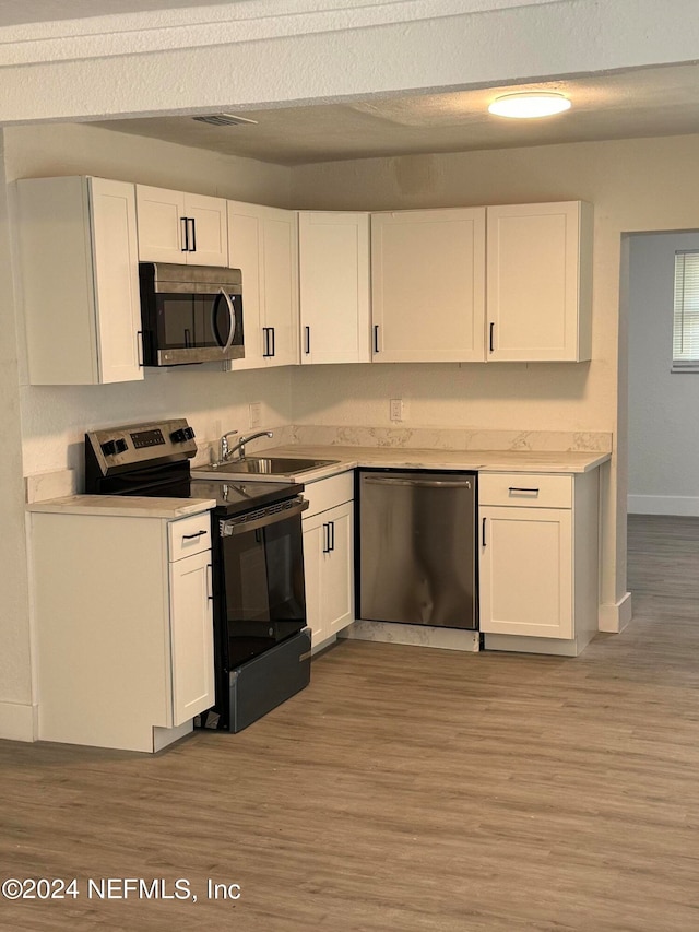 kitchen featuring white cabinets, appliances with stainless steel finishes, light wood-type flooring, and sink